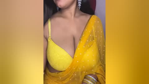 Media: Video of a South Asian woman with medium brown skin, wearing a yellow polka-dot saree and a matching bra, with a gold bracelet on her wrist.