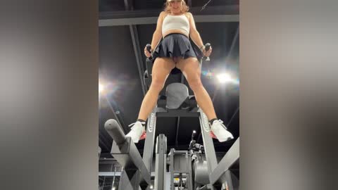 Media: A video of a fit Caucasian woman in a sports bra and short skirt, performing a squat on a gym machine, with studio lighting creating a dramatic, slightly blurred background.