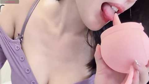 Media: Video of an East Asian woman with light skin, wearing a lavender off-shoulder top, licking a pink bra. Her breasts are partially visible, emphasizing her cleavage.