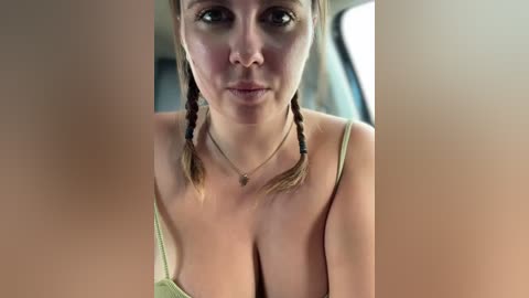 Media: Video of a fair-skinned woman with brown hair in braids, wearing a beige camisole, smiling seductively in a car.