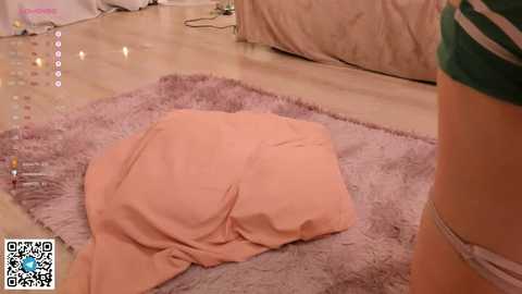 Media: Video of a light-skinned person lying on a pink shag rug in a room with beige walls and a green-striped shirt visible.