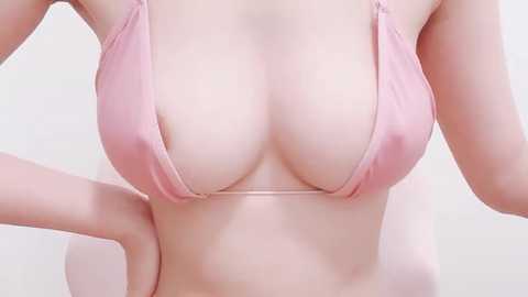 Media: Video of a light-skinned woman's upper torso in a pink bikini top, showcasing medium-sized breasts. She has her hands on her hips, with a plain white background.