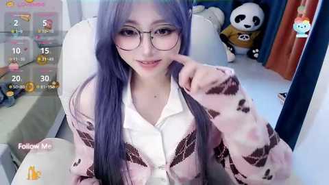 Media: Video of a young woman with long purple hair, wearing glasses, a white blouse, and a pink cardigan, seated in a room with a panda plush toy and gaming elements.