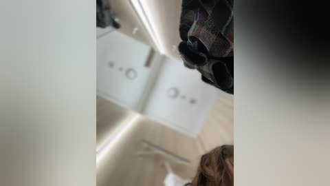 Media: Video of a bathroom mirror reflection showing a person's face with brown hair and a plaid shirt, and the back of a white toilet with a lid.