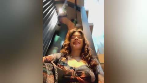 Media: A video of a smiling woman with curly hair, wearing a colorful floral shirt, descending a staircase. The background features blurred stairs and a blue wall.