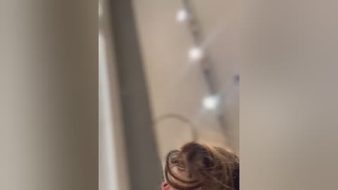 Media: A video of a child with brown hair and a curious expression, looking up from the bottom of the frame, in a dimly lit hallway with blurred, beige walls and a string of lights.