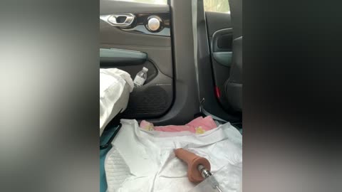 Media: Video of a car interior with a person working under the driver's seat, using a wrench on a metal part. The scene is messy with tools, plastic bags, and white towels scattered on the floor.