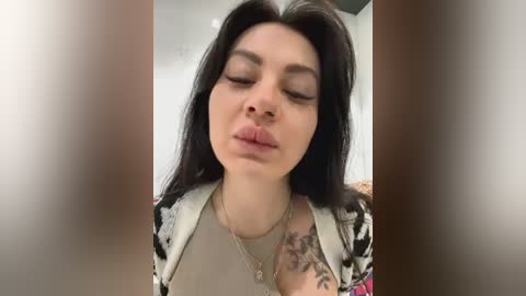 Media: Video of a woman with fair skin, long dark hair, closed eyes, pursed lips, and a floral-patterned top, featuring a large floral tattoo on her left shoulder.