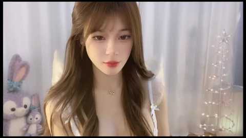 Media: Video of a young East Asian woman with long brown hair, pale skin, and light makeup, wearing a white lace top, standing in front of sheer curtains with a plush bunny toy.