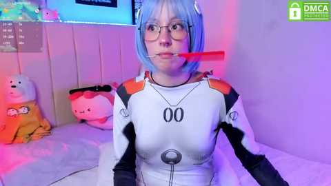 Media: Video of a light-skinned woman with blue hair and glasses, wearing a white Evangelion cosplay suit with a gag, standing in a colorful, neon-lit room with plush toys.