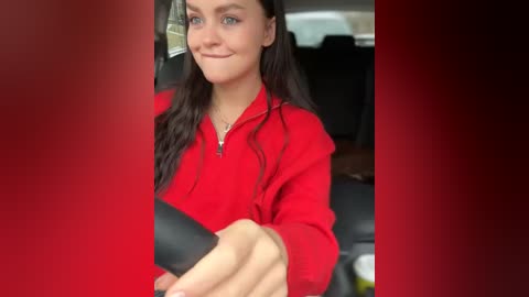 Media: A video of a smiling woman with long dark hair, wearing a bright red jacket, driving a car. The background shows a blurred interior of a car with black seats.