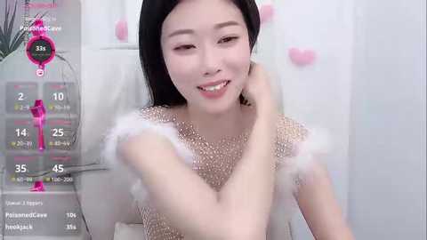 Media: Video of an East Asian woman with long black hair, fair skin, and a smile, wearing a sparkly, white, feather-trimmed dress. Background includes a pink heart and a digital display with her stats.