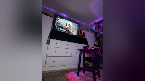 Media: Video of a dimly lit bedroom with a white dresser, TV displaying a video game, purple LED strip lights, and a chair with a pink drink.