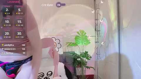 Media: Video of a person wearing a floral dress, bending over a plant in a room with a colorful, abstract wall painting and a pink plant in a pot.