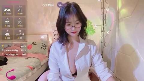 Media: A video of an East Asian woman with shoulder-length black hair and glasses, wearing a white shirt unbuttoned to reveal cleavage, sitting in a cozy, pastel-themed bedroom.