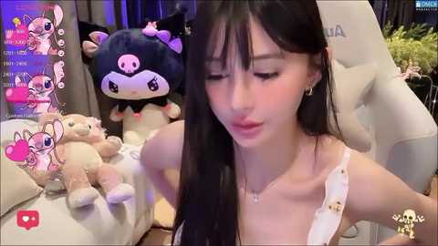 Media: A video of a young East Asian woman with long black hair, wearing a white camisole, sitting on a plush chair. The background features plush toys and virtual chatroom elements.