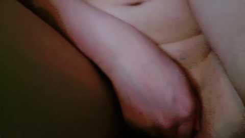 Media: A close-up video of a nude person's arm and torso, with the focus on the hand covering the genitals. The skin tone is light with a slight pinkish hue. The background is blurred, focusing attention on the intimate, private moment.