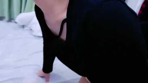 Media: Video of a woman in a black dress bending over, revealing cleavage, on a light-tiled floor. Green curtains and white pillow in the background.