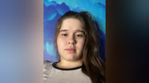 Media: Video of a young Caucasian girl with long brown hair, fair skin, wearing a gray and white striped shirt, against a blue and purple abstract background.