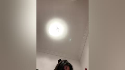 Media: Video of a ceiling light shining brightly in a corner of a room with white walls and a dark-haired person's head visible below.