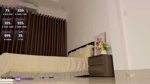 Media: Video of a minimalist bedroom with beige bedding, dark curtains, a wooden nightstand with a vase of flowers, and a digital display showing temperature and humidity levels.