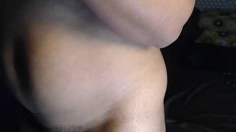 Media: Video of a close-up of a bare, light-skinned shoulder and upper back, with a blurred, dark background suggesting an indoor setting.