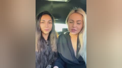 Media: Video of two women in a car, one with long, straight, dark hair, the other with blonde, wavy hair. They wear dark, formal clothing. Background shows car interior.