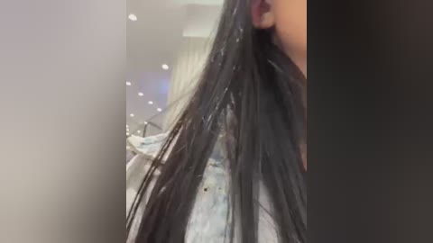 Media: A video showing a close-up of a woman's shoulder and neck, with long, dark brown hair wet and slicked back. She wears a light denim jacket. Background is blurred, featuring a salon setting with soft lighting and a blue tint.