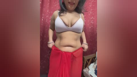 Media: Video of a curvy, light-skinned woman with blue hair, wearing a white bra and red sarong, standing in a dimly lit room with red curtains.