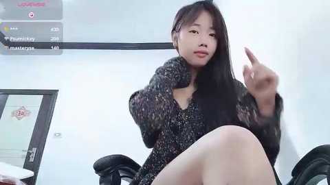 Media: Video of an East Asian woman with long black hair, wearing a black fur-trimmed sweater, seated in a black office chair, flipping the bird, with a digital board displaying prices in the background.