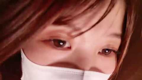 Media: Close-up video of an Asian woman with fair skin, brown hair, and brown eyes, partially obscured by a white surgical mask, creating a sense of tension and mystery.