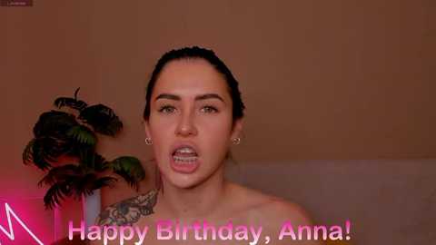 Media: A video of a woman with dark hair pulled back, wearing small hoop earrings, and a colorful tattoo on her shoulder, with a caption reading \"Happy Birthday, Anna.\