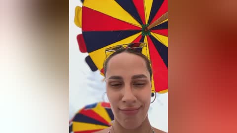 Media: Video of a smiling woman with light brown skin, wearing a colorful, patterned umbrella as a hat, against a white background.