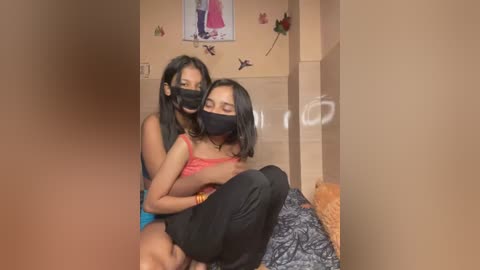 Media: Video of two young women with dark skin, one in a black mask, holding the other who is topless, wearing a pink bra.