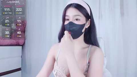 Media: Video of an Asian woman in a hospital gown with a mask, holding a thermometer. Background shows a digital thermometer display and white curtains.