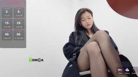 Media: Video of an East Asian woman with long black hair, sitting in a white room, wearing a black blazer, and looking tired.