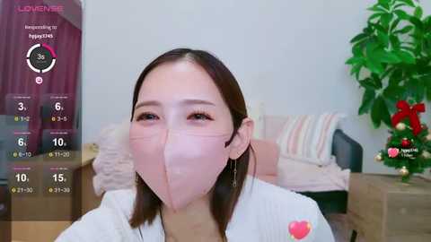 Media: Video of an East Asian woman in a white shirt, wearing a pink face mask, with a thermometer in the corner.