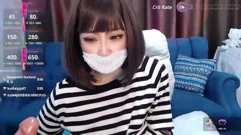 Media: A video of an Asian woman with straight, shoulder-length brown hair, wearing a black and white striped shirt and a white mask, sitting in a blue couch, surrounded by digital stats and social media icons.