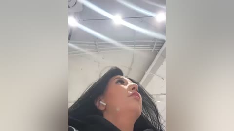 Media: A video of a woman with long black hair, wearing white wireless earbuds, looking upward in a white-walled room with a ceiling fan, beams of light shining through.