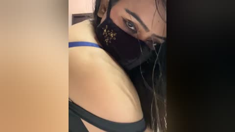 Media: A close-up video of a person with dark skin and long, wet hair, wearing a blue and black mask, black bra, and a dark top, partially obscured by their hair, in a dimly lit room.