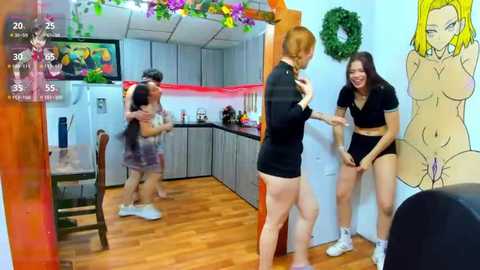 Media: A lively video shows two young women, one with short red hair, in a kitchen, playfully grabbing each other's breasts. The room is colorful, with a cartoon mural and wooden floor.