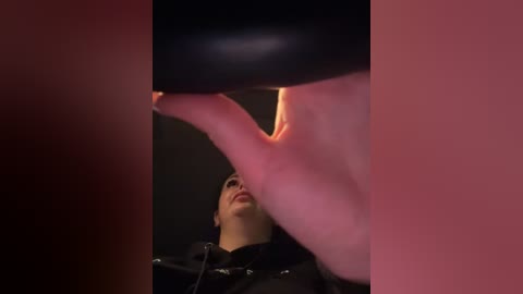 Media: A video shows a close-up of a black strap-on dildo being inserted into a person's mouth. The background is blurred, with a mix of pink and red hues. The image has a voyeuristic and intimate feel.