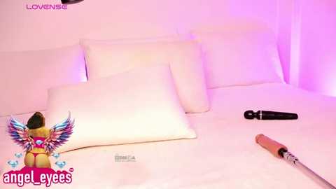 Media: Video of a bed with white sheets, featuring a plush white pillow and a small, colorful angel figurine with wings. A black vibrator and a pink vibrator are on the bed, set against a soft pink background.