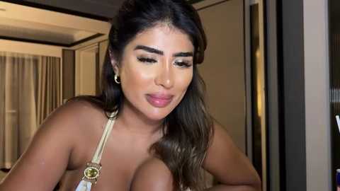 Media: Video of a Latina woman with long dark hair, wearing a beige lace bra, in a well-lit bedroom with beige curtains and a mirrored wardrobe.