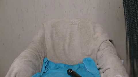 Media: A video showing a person in a beige t-shirt and blue jeans lying on a beige couch, with a blue blanket covering their legs, and a black bottle on the floor.