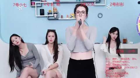 Media: Video of four Asian women in casual outfits, one with a microphone, in a modern living room with shelves and a clock.