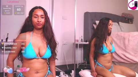 Media: Video of a young, fit, black woman with long, wavy hair, wearing a bright turquoise bikini, sitting on a bed in a cluttered bedroom.