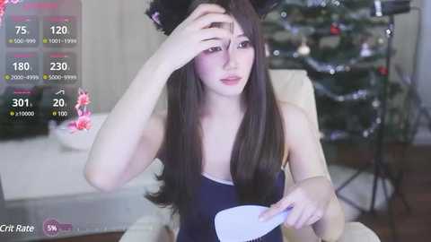 Media: Video of an Asian woman with long black hair, wearing a black top and bunny ears, sitting in a dimly lit room with a Christmas tree in the background.