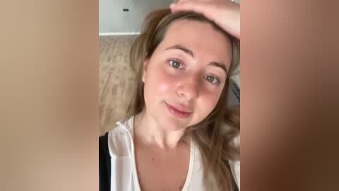 Media: Video of a young woman with fair skin, light brown hair, and green eyes, smiling, laying on a beige carpet, wearing a white shirt.