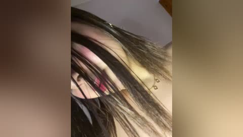 Media: A close-up video of a young woman with long, dark hair partially covering her face, wearing a black top, and a hint of a pink lipstick. The background is blurred.